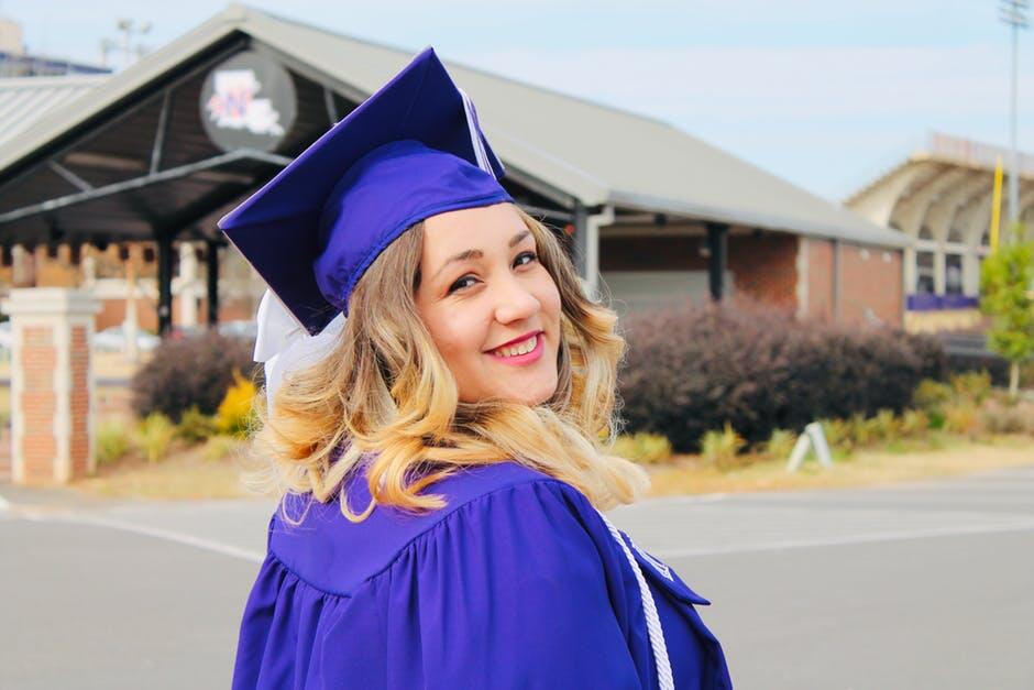 A graduate of higher education smiling and looking over shoulder at the camera